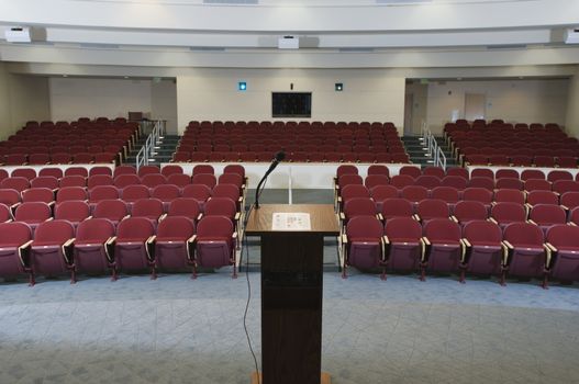 Red chairs arranged in order and podium at an empty conference auditorium