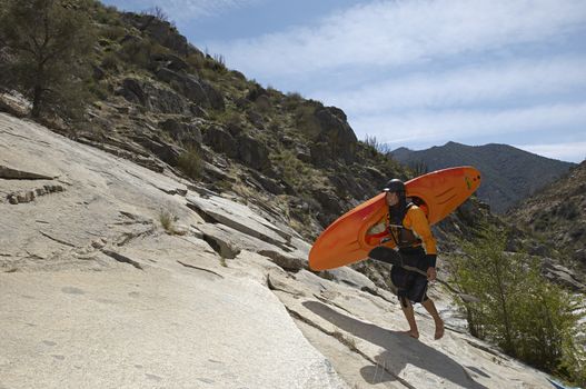 Full length of a female kayaker with vessel and oar walking on rock