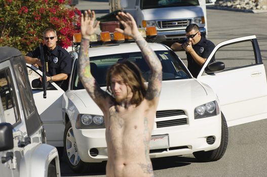 Two police officers aiming guns at shirtless young man