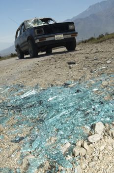 Close-up of broken windshield pieces on ground with damaged truck in background