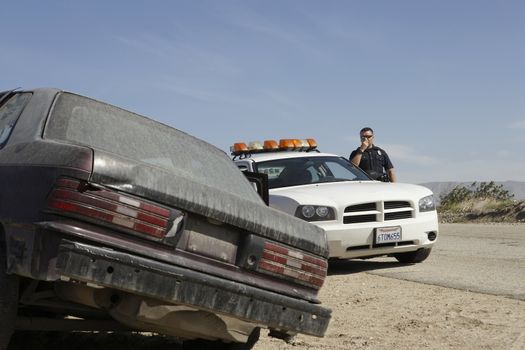 Police officer using CB radio near abandoned car on desert road