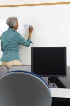 Female teacher writing on whiteboard in computer class
