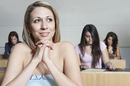 Young female student daydreaming during lecture with classmates in background