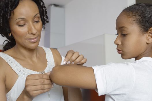 Closeup of an African American mother applying bandage on daughter's hand