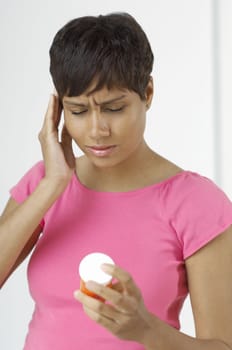 An African American woman with severe headache holding pill bottle