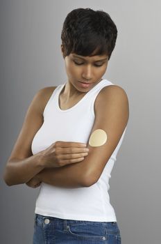 An African American woman with nicotine patch on arm over grey background