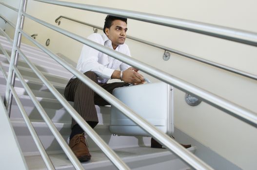 An Indian businessman contemplating while sitting on stairway