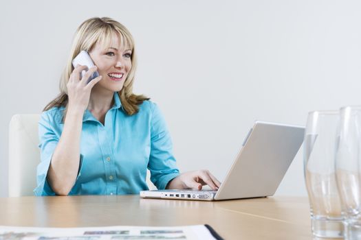 Happy Caucasian business woman on call while using laptop at office