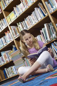 Girl sitting on the floor and reading book in library tilt