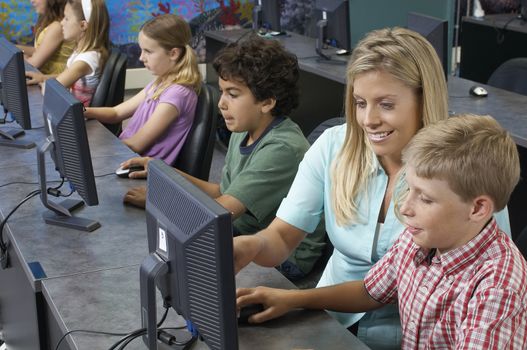 School children using computers with teacher in classroom