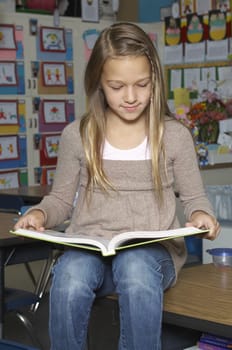 School girl reading book on desk in classroom