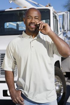 Mid-adult truck driver on the phone in front of a truck