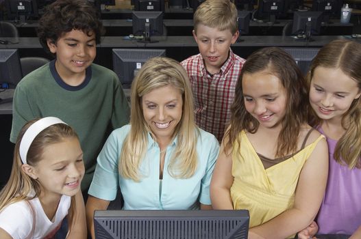 School children using computer with teacher in classroom
