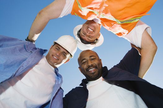 Construction workers forming a huddle against blue sky