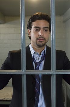 Mid-adult businessman standing behind cell bars