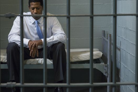 Businessman sitting in prison cell