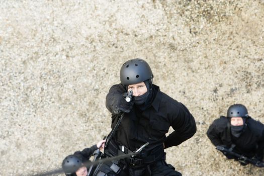 Portrait high angle shot of a SWAT team officer rappelling and aiming gun