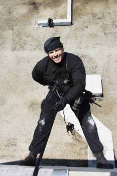 Full length of a smiling SWAT team officer rappelling from building