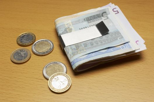 European currency in silver money clip and coins on wooden table