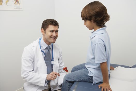 Mid-adult doctor examining boy with reflex hammer