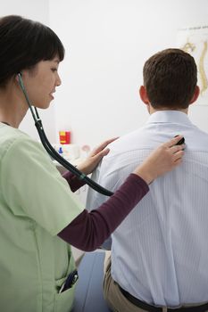 Doctor examining male patient using stethoscope in hospital