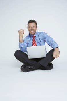 Studio portrait of businessman sitting with laptop and punching air