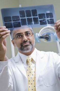 Male Asian dentist examining x-ray report in clinic