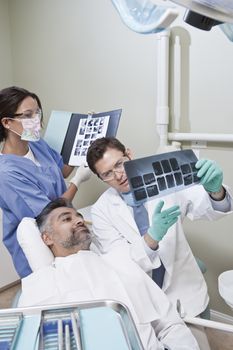 Male dentist and nurse explaining x-ray report to patient in clinic