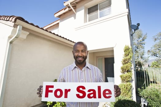 Portrait of an African American estate agent holding ~For Sale~ sign against house