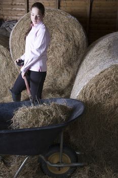 Girl shoveling hay in barn
