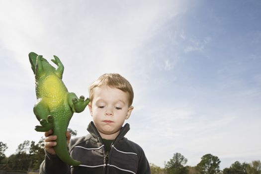 Displeased boy holding toy dinosaur