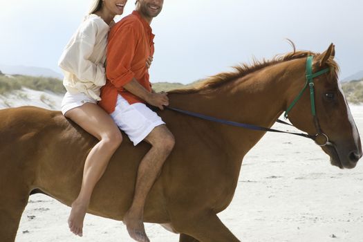 Mid-adult couple riding horse on beach