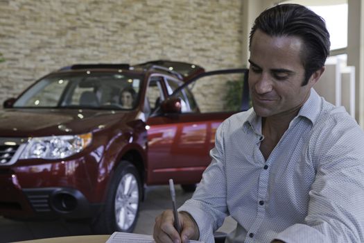 Man signing papers with car in background