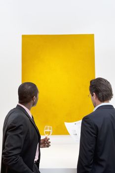 Two people looking at yellow painting on wall in art gallery
