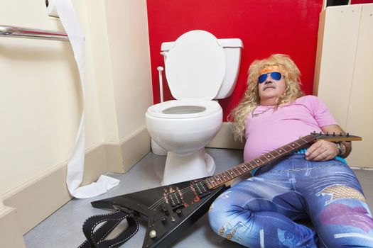 Man lying down in toilet with a guitar