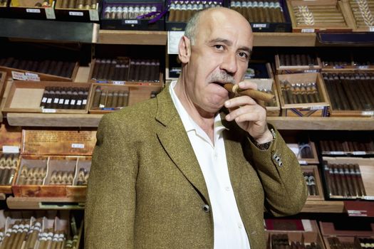 Portrait of mature tobacco shop owner smoking cigar in store