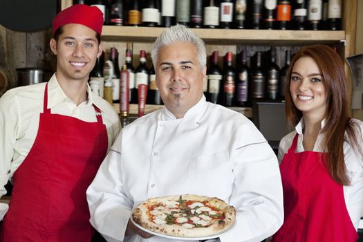Portrait of a happy chef holding pizza with wait staff