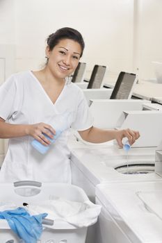Portrait of a happy woman employee pouring detergent in washer