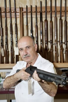 Mature gun merchant with rifle looking away