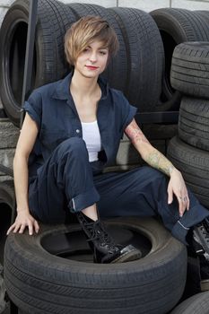 Portrait of a young mechanic sitting on tires in car workshop