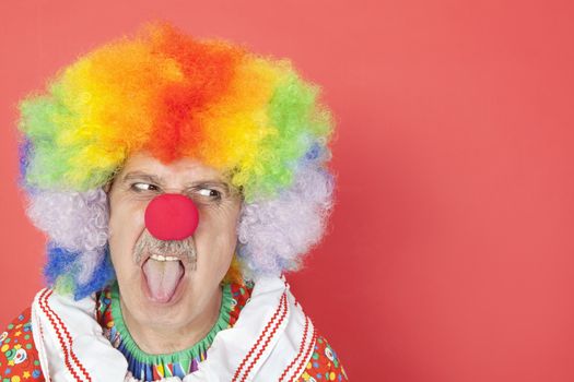 Senior male clown sticking out tongue while looking away over red background