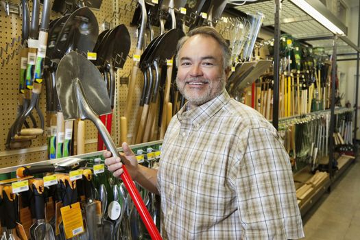 Portrait of a happy mature man holding shovel in hardware store