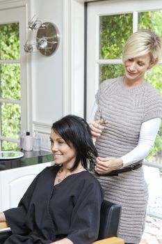 Beautiful happy woman getting a haircut from a mature hairstylist in beauty salon