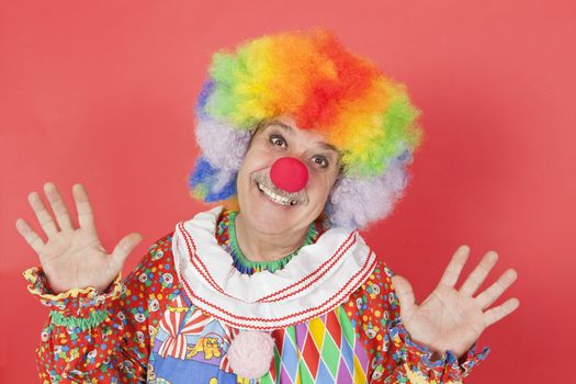 Portrait of funny clown with arms raised against colored background