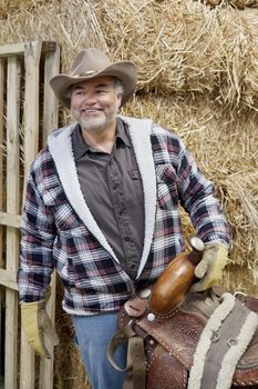 Happy mature cowboy holding saddle
