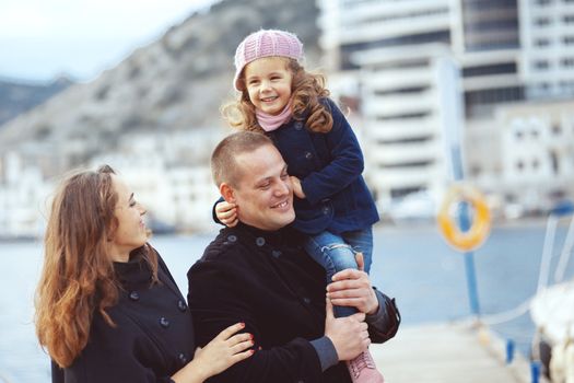 Portrait of happy young family walking with their child on berth near sea in the city, still life photo