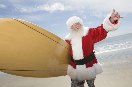 Father Christmas stands with a surfboard at the beach