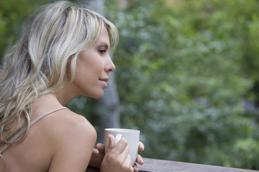 Blonde woman sits with cup on garden veranda