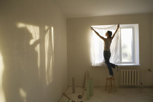 Woman fitting curtains in new apartment
