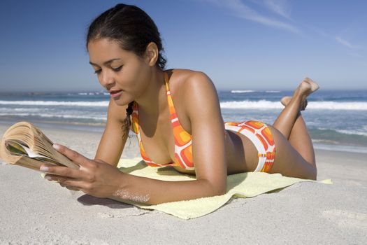 Young woman in retro swimwear lies on beach reading a book